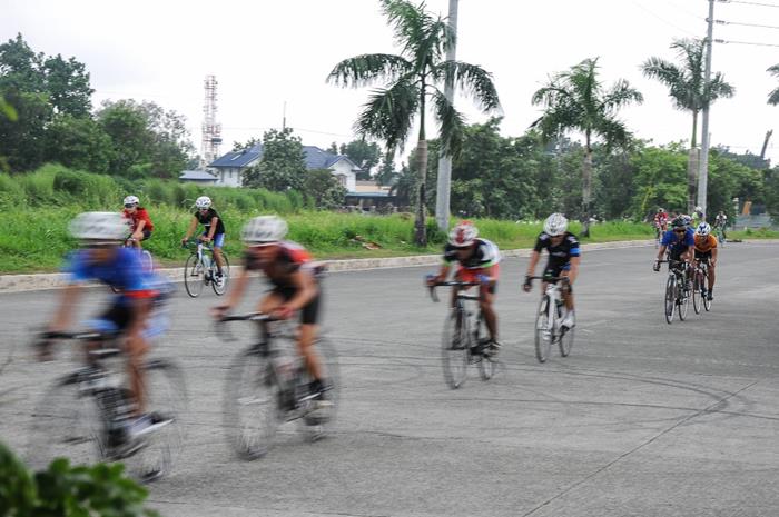 Two junior triathletes warm up on the side as the race peloton whizzes past