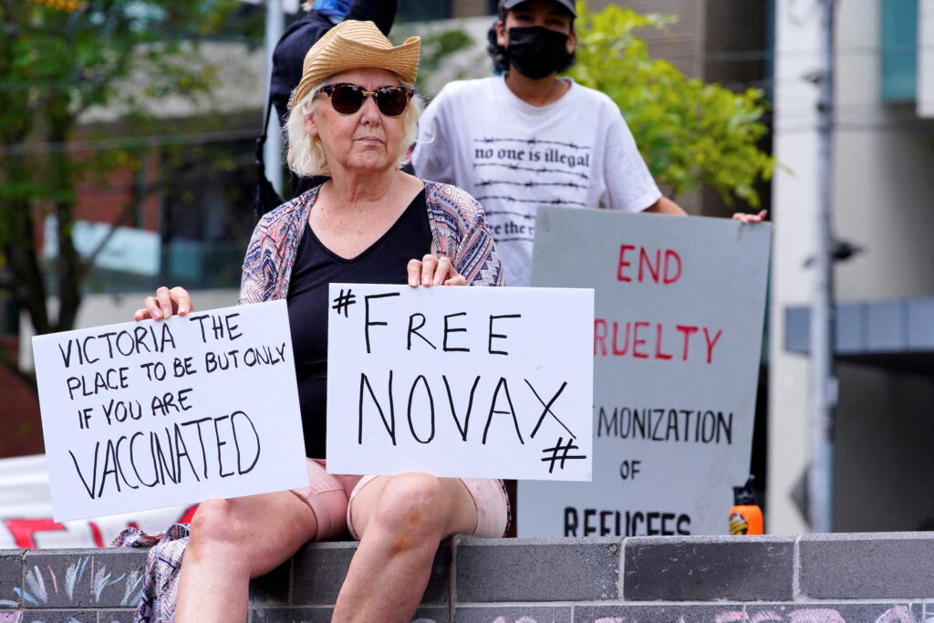 A protester holds signs outside the Park Hotel, where Serbian tennis player Novak Djokovic is believed to be staying in Melbourne, Australia